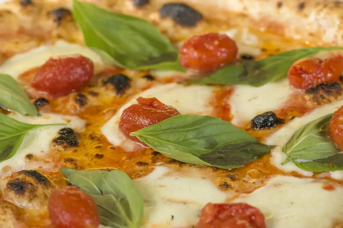 Pizza mit geschmolzenem Mozzarella, Basilikum und gerösteten Kirschtomaten in Nahaufnahme