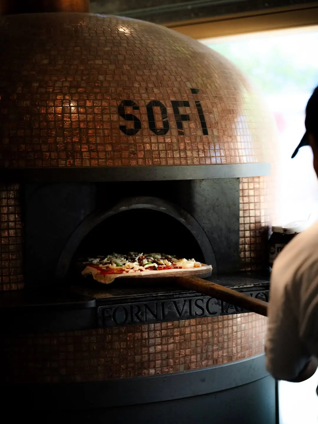 Eine Pizza wird in den mosaikverzierten SOFI Ofen geschoben